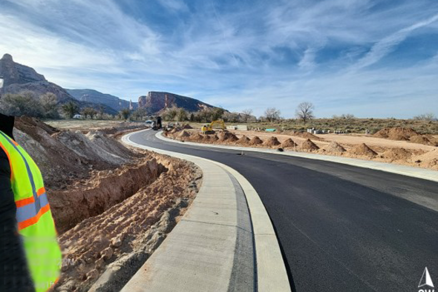 A construction worker's perspective of a new road and sidewalk curving into the distance towards rocky hills.