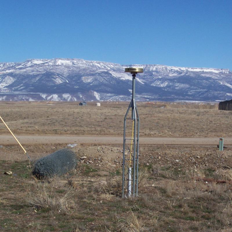 GPS choke ring antenna pushed into the desert ground with a snow covered mountain in the background. 