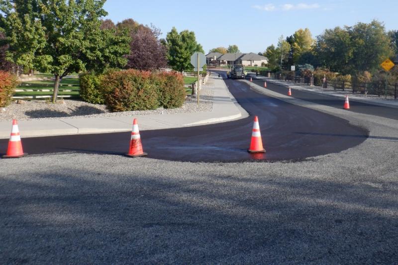 Newly paved black road with orange cones on it. 