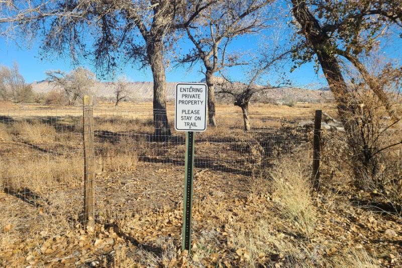 A sign reading 'Entering Private Property, Please Stay on Trail' stands near a wire fence in a rural setting near the Clifton Nature Park.