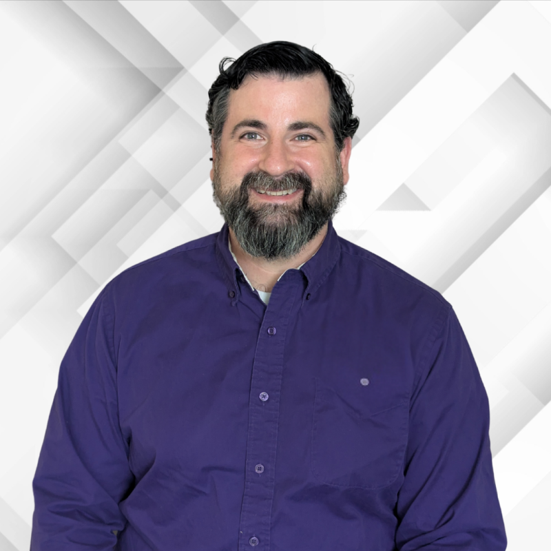 Smiling man with dark hair and beard in a purple shirt.