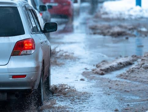 A silver car driving through a partially flooded road due to snow melt.
