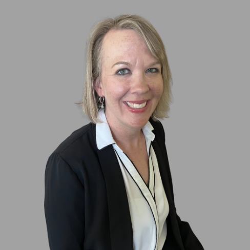 A person in a black blazer and white blouse smiles at the camera.