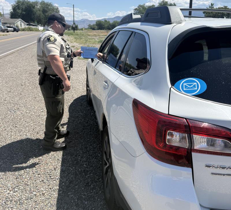 Deputy being handed a blue envelope from driver of a parked vehicle