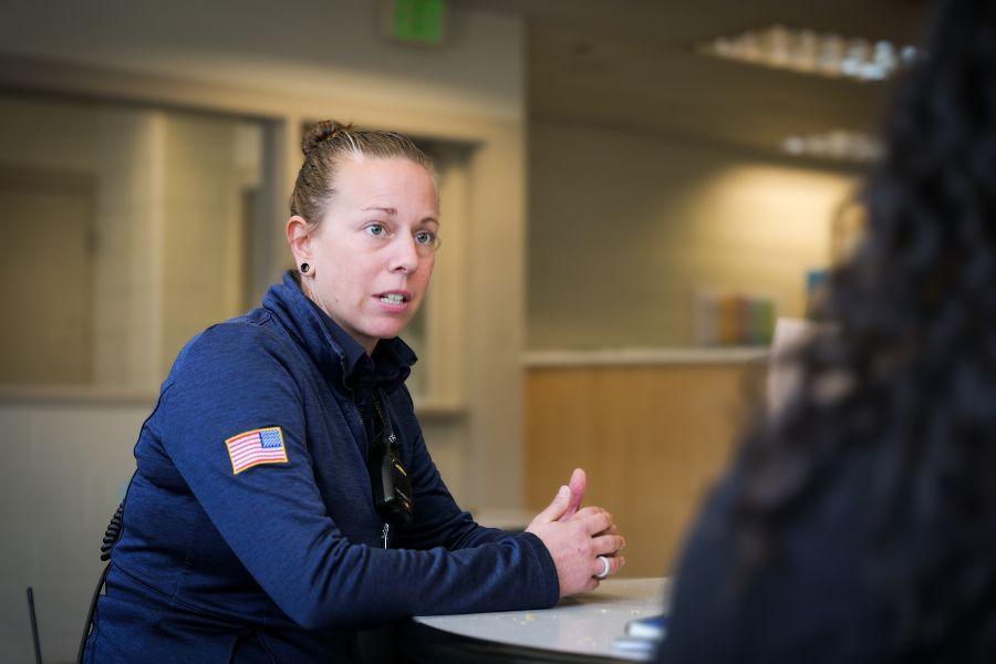 Woman in blue Criminal Justice Services uniform sits at a table facing a woman in a black shirt. 