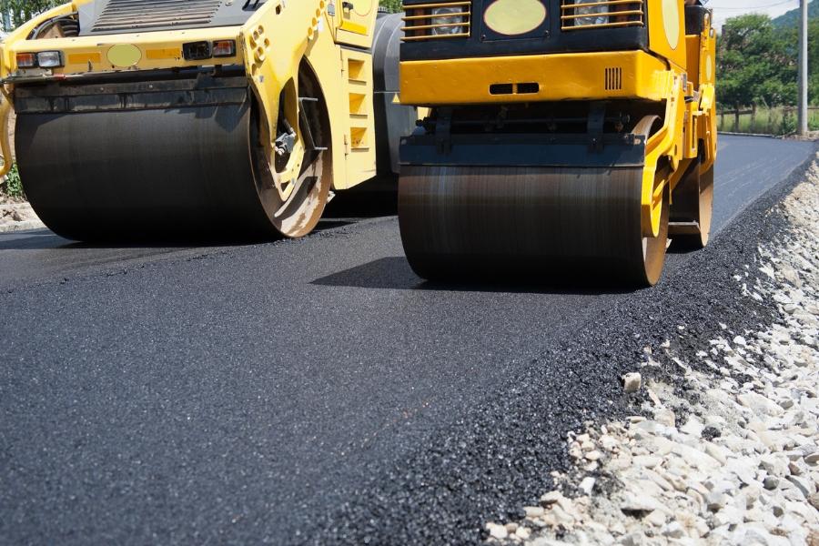 Yellow heavy construction equipment rolling over fresh black asphalt. 