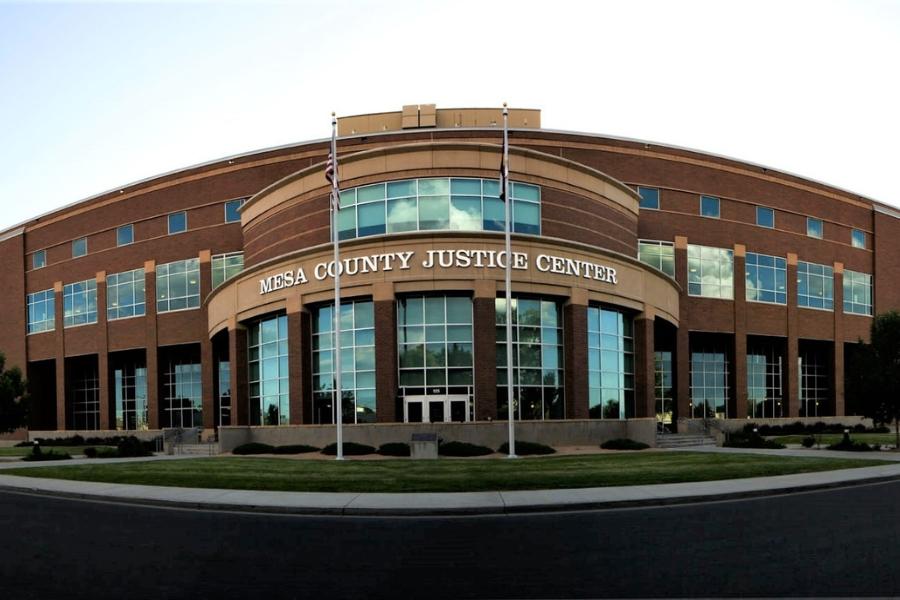 Large brick building with white sign reading, Mesa County Justice Center and two flags in front of it. 