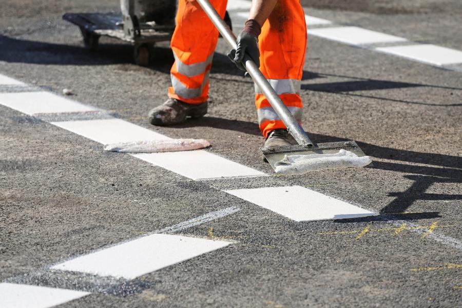 Construction worker painting white lines on a road, from the knees down. 