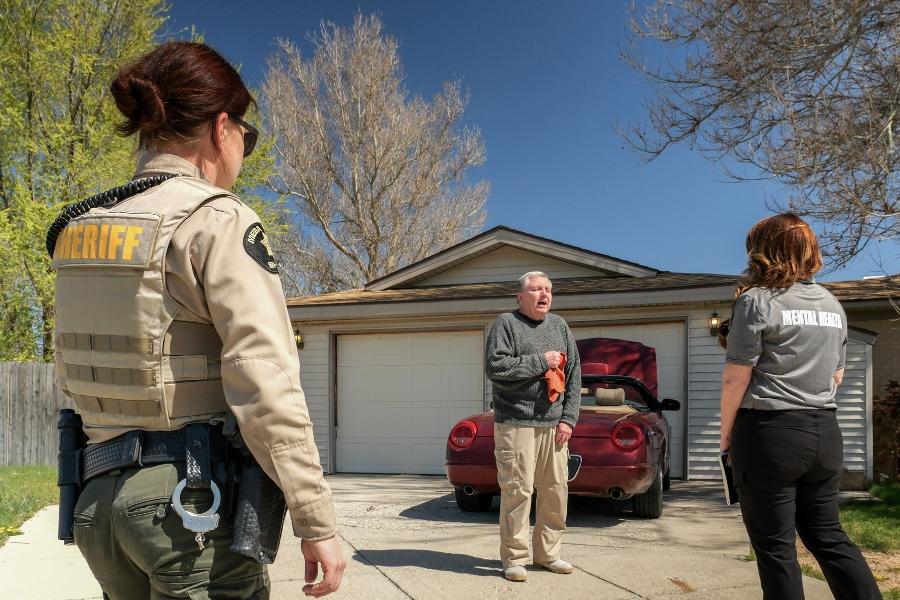Back of Sherriff's deputy and mental health professional helping person. 