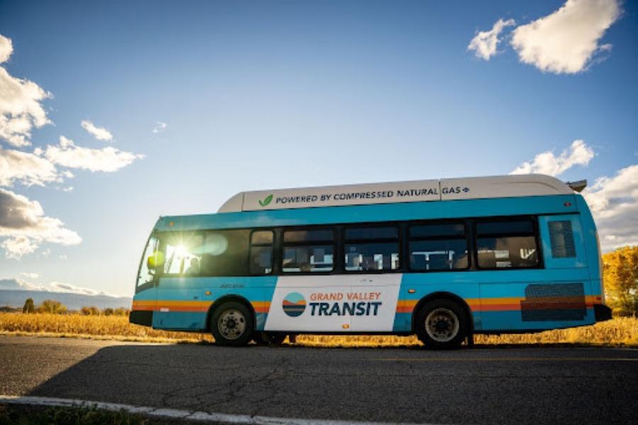 Blue, orange, and yellow bus drive on paved road during sunset. 