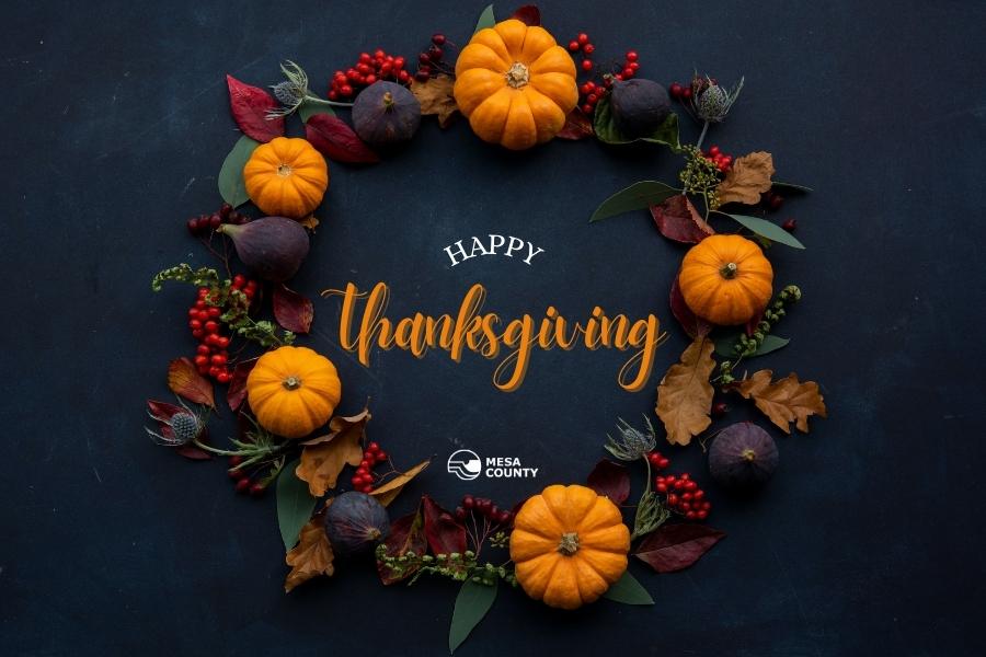 Blue background with wreath covered in pumpkins and berries and white and orange text in the middle reading, "Happy Thanksgiving."