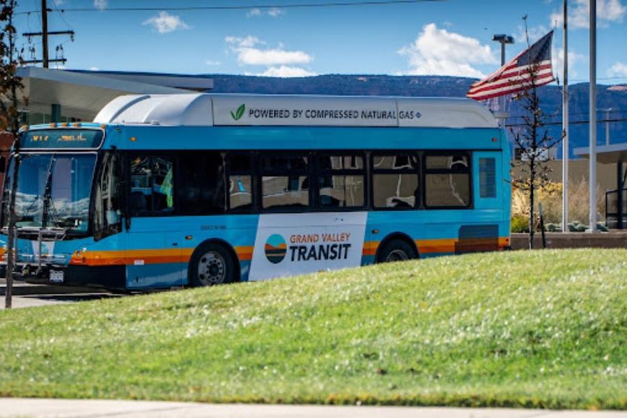 Blue /Grand Valley Transit bus behind grass next to an American flag. 
