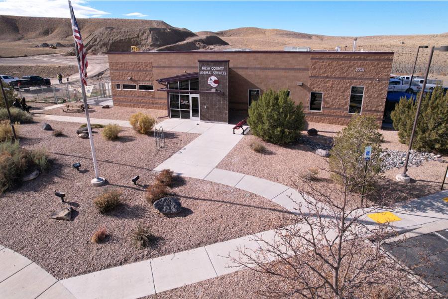 Wide view of brick building with white sign reading, "Mesa County Animal Services," with the red and white Animal Services logo and an American flag outside the building. 