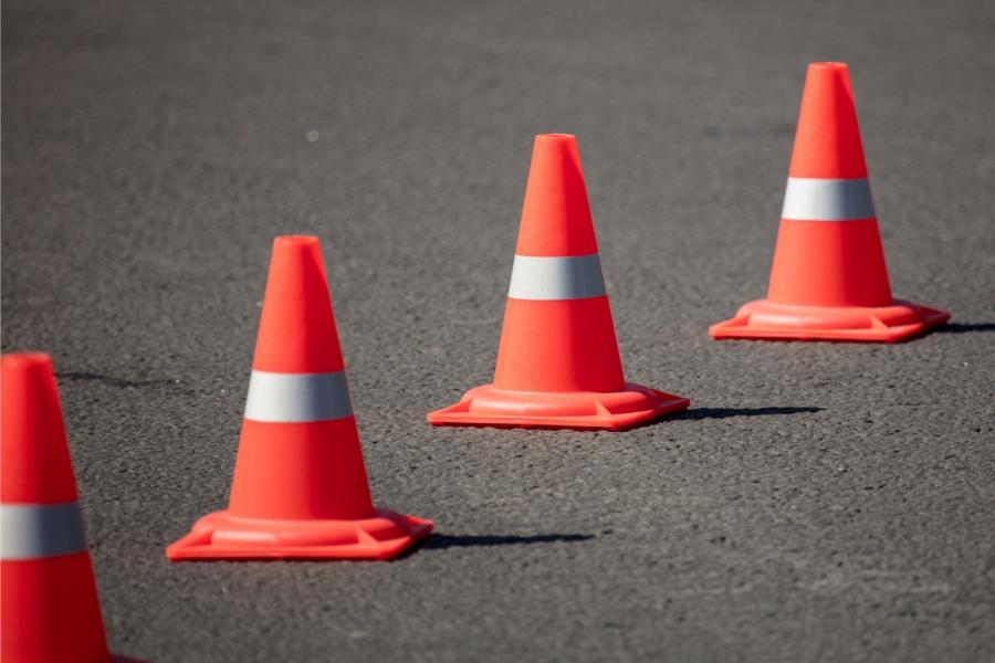 Four orange and white construction cones on black road. 