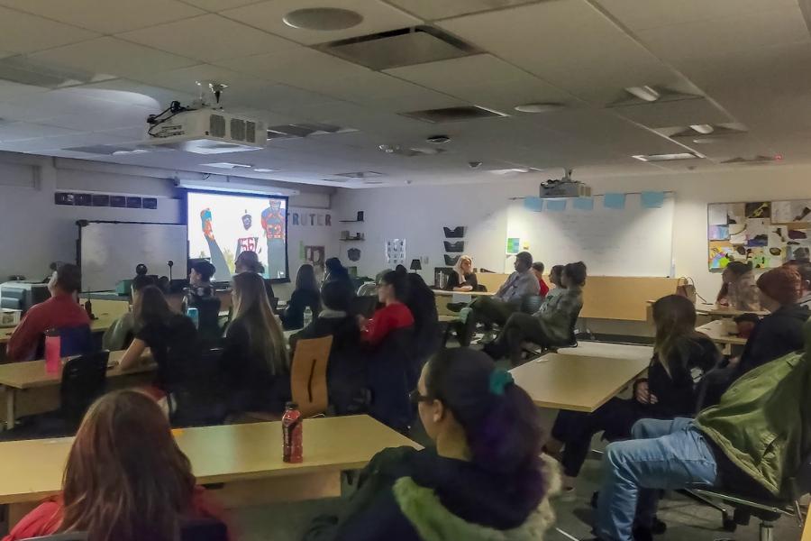 Children and parents sitting in classroom facing a projected screen showing two football players. 