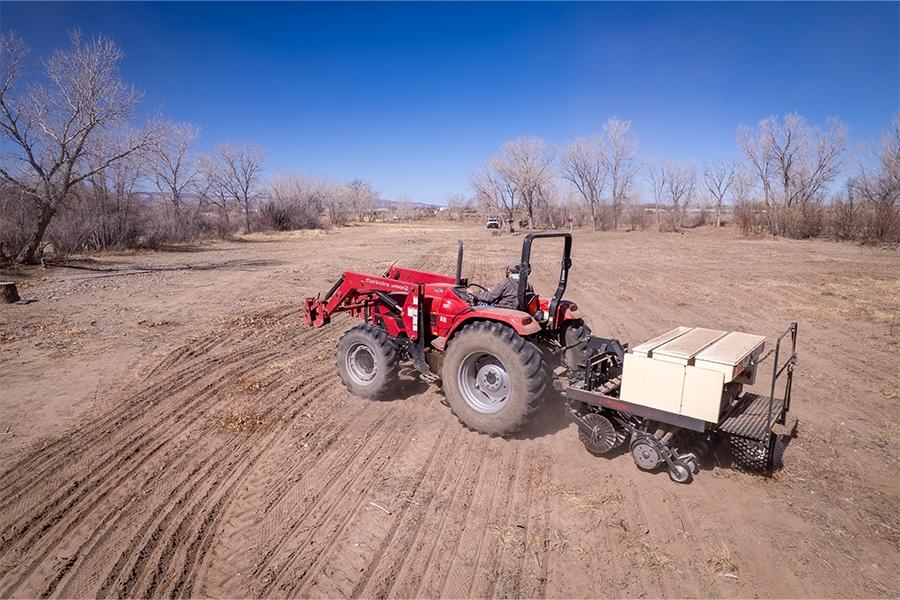 A person drives red heavy equipment over dirt to perform drill seeding. 