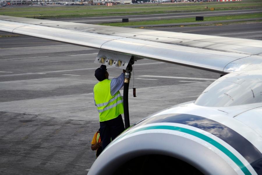 The back of a man wearing a bright yellow vest putting fuel into and airplane. 