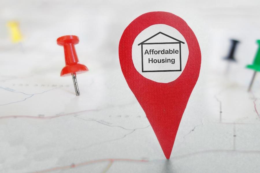 A blurred map with several colored tacks marking different locations and a larger red pin that reads Affordable Housing. 