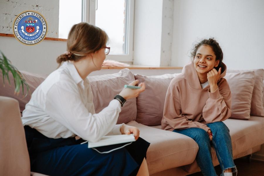 A child and an adult sitting on a couch talking. 