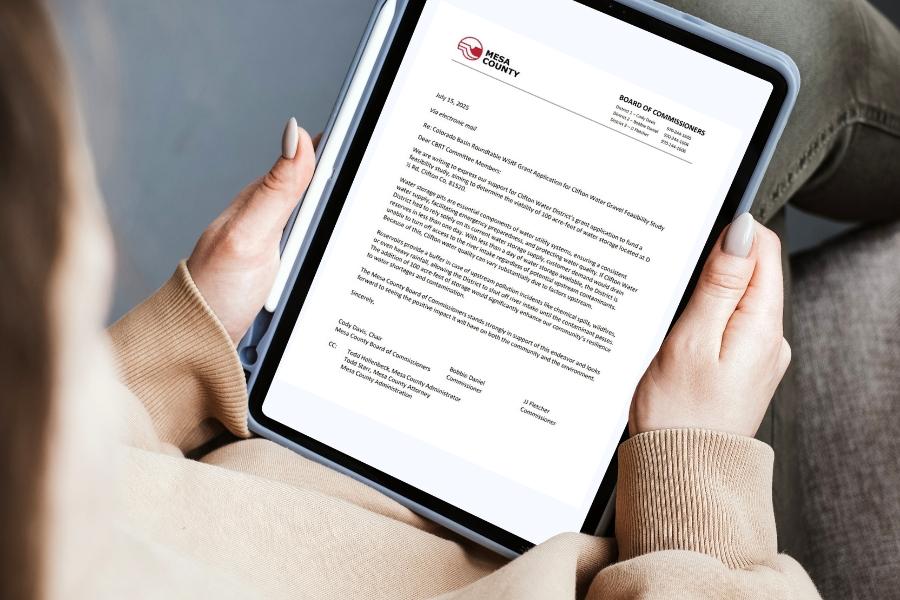 Hands holding an iPad displaying a Mesa County letter. 