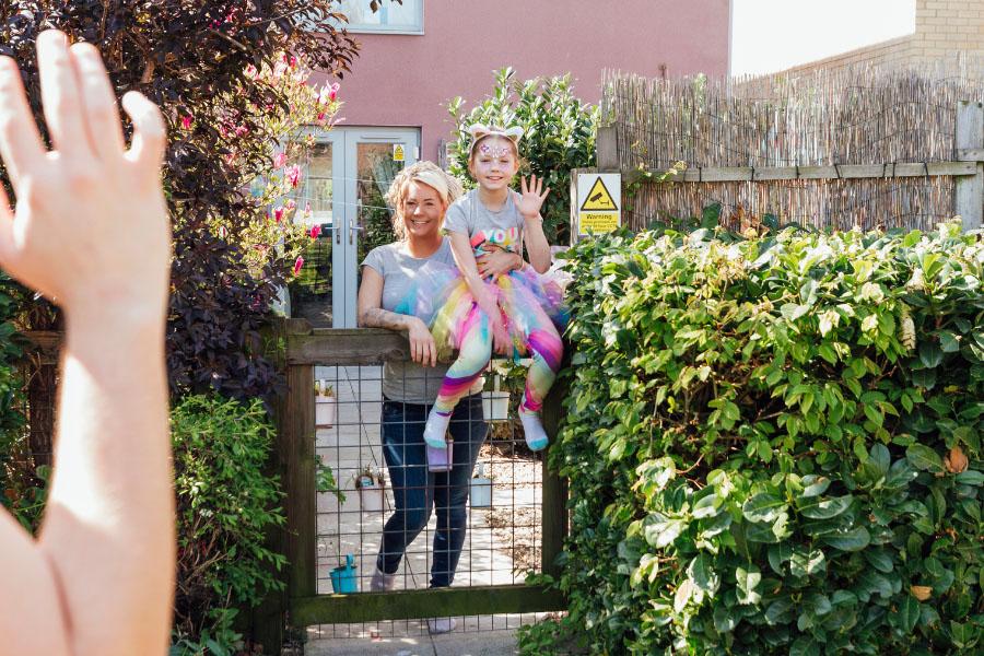 Mother and child waving goodbye from a fence in their yard.