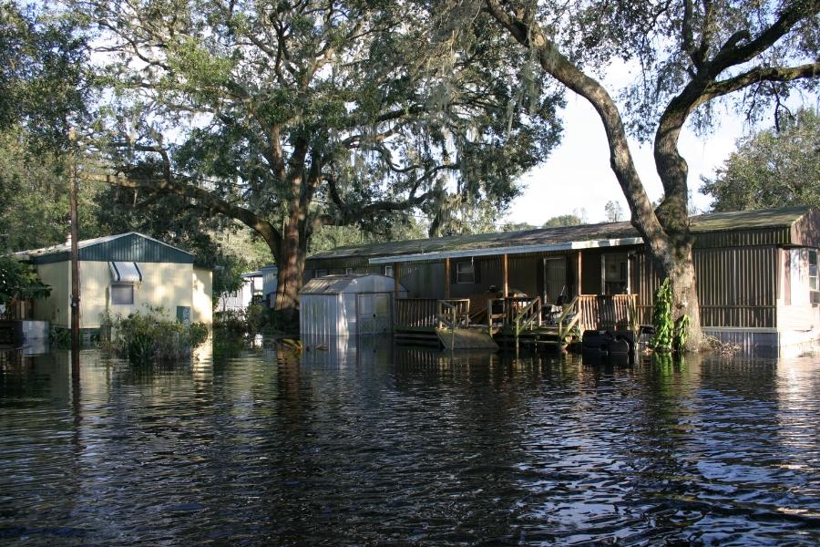 A flooded road near two houses and trees.