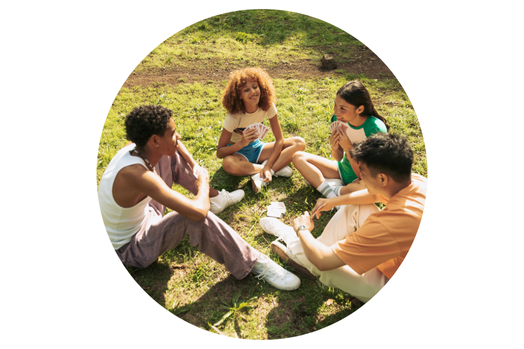 Four teenagers sitting in a circle on grass playing cards