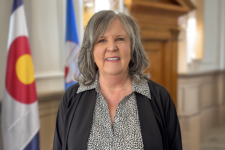 Portrait of Arna Hoffman, newly appointed Mesa County Treasurer, standing indoors with the Colorado state flag and Mesa County flag in the background.