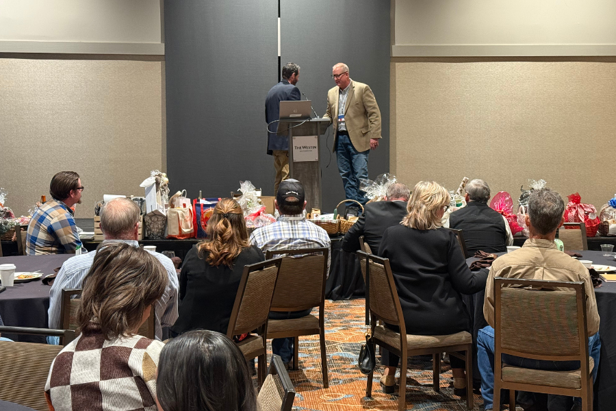 Attendees sit at round tables facing a small stage where ​Mesa County Administrator Todd Hollenbeck is being recognized at a podium during ​CCI's winter conference.