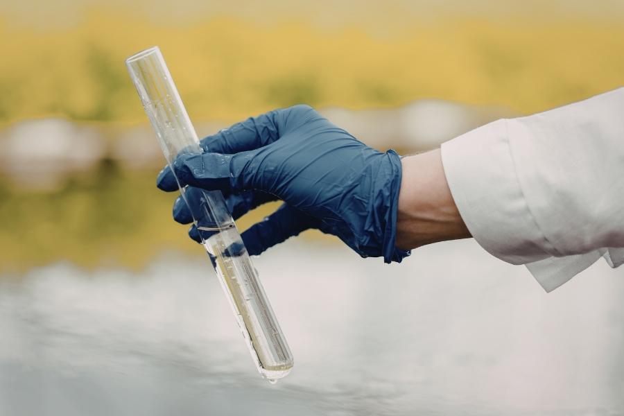 A hand wearing a blue glove holding water in a test tube.