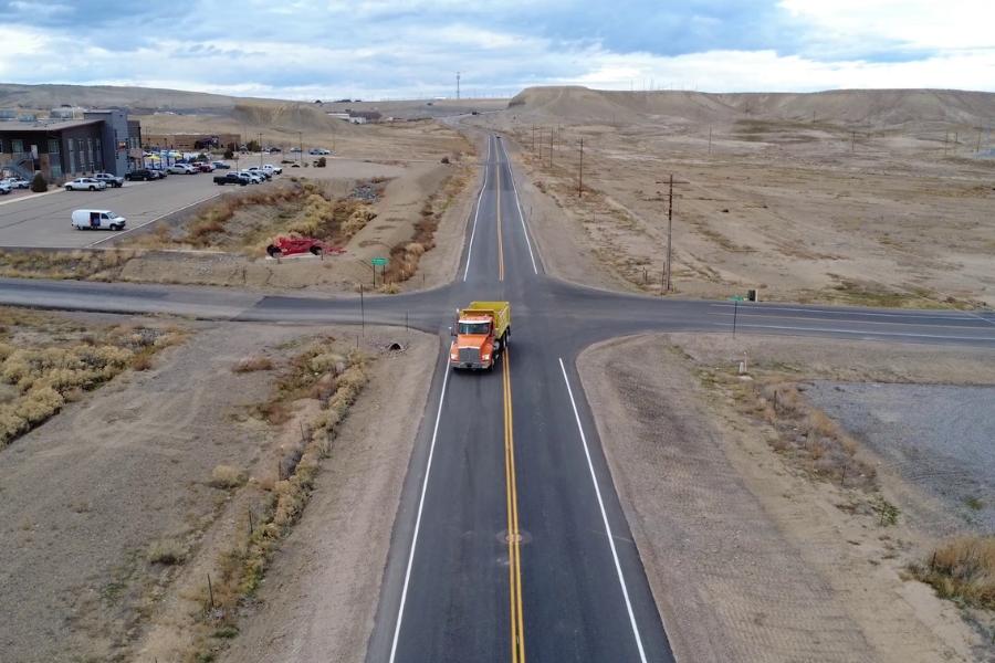 An orange truck driving down a newly improved road. 