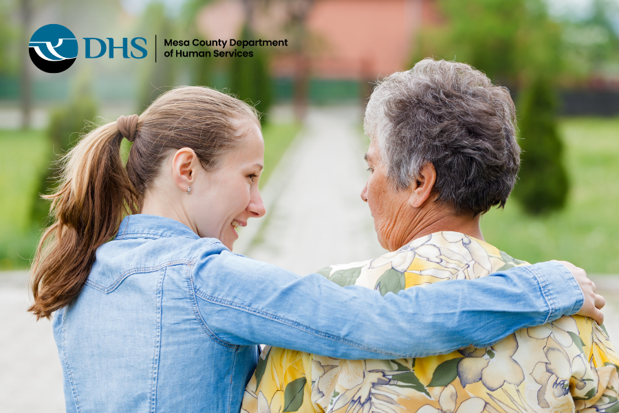 A younger woman embracing an elder with their backs to the camera and walking away. MCDHS logo in top left