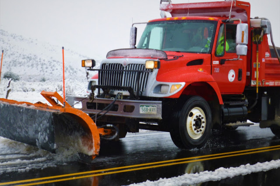 A red Mesa County snowplow truck pushes snow off a wet roadway during winter conditions, illustrating how county crews maintain road safety during snowstorms.