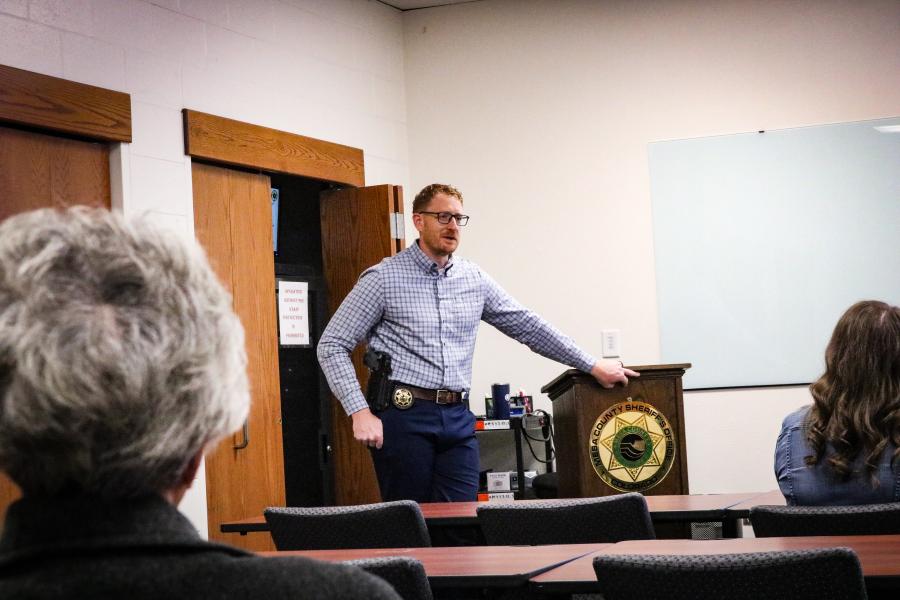 Sheriff's Office investigator speaking to a room of citizens, leaning on a podium with the agency logo on it.