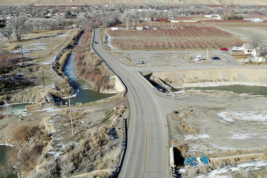 Aerial view of 38 Road crossing the Orchard Mesa irrigation channel, showing the narrow roadway, adjacent open canal, surrounding farmland and limited space for pedestrians and cyclists.