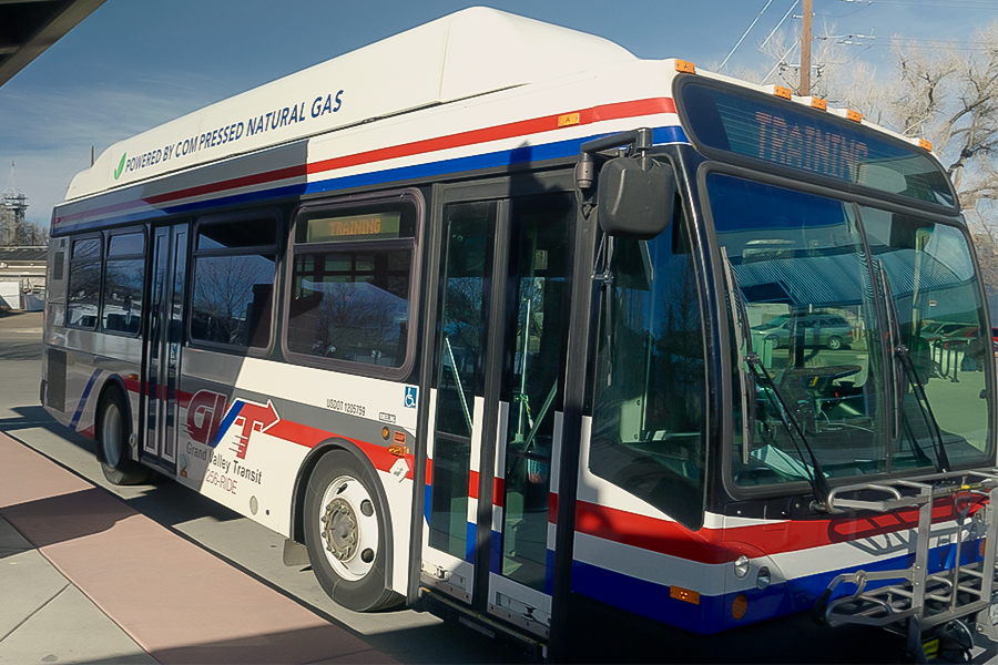 A Grand Valley Transit bus powered by compressed natural gas is parked at a curb, with red, white and blue striping.