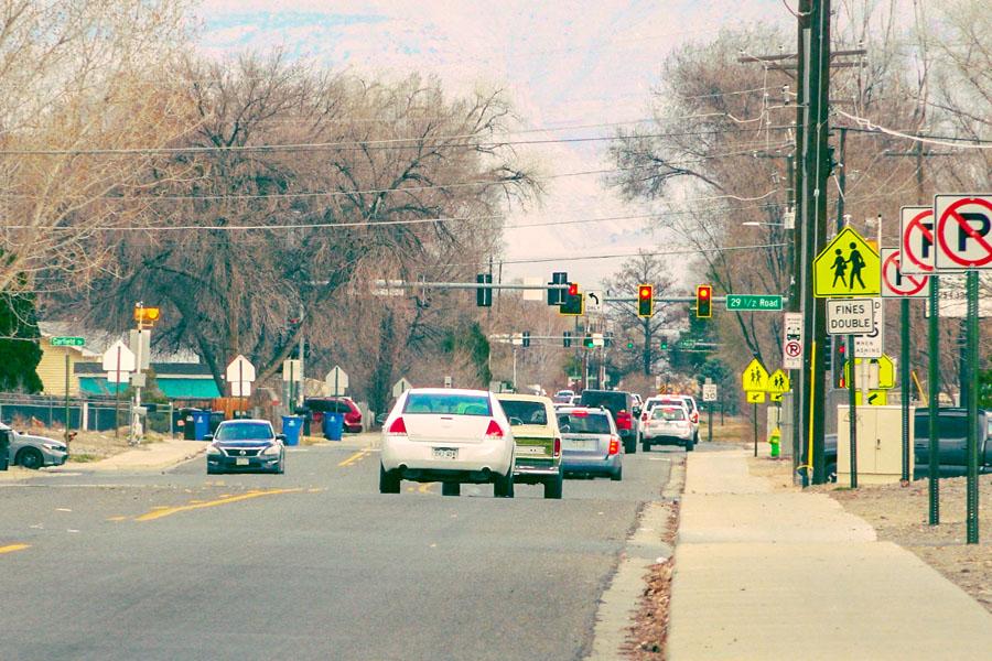 Vehicles travel along Orchard Avenue approaching the intersection at 29 1/2 Road, with traffic signals, crosswalk signs and sidewalks visible along the corridor.