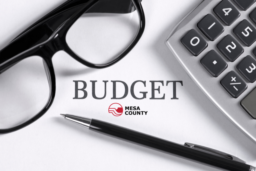 The word "Budget" on a document with the Mesa County logo, alongside a pair of glasses, a pen and a calculator on a desk.