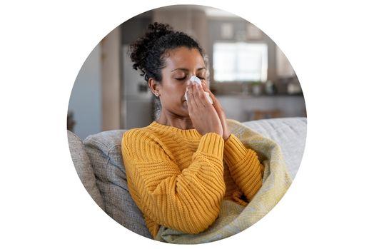 A person sitting on a couch wrapped in a blanket, holding a tissue to their nose.