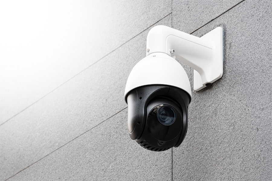 A mounted security surveillance camera is attached to the exterior wall of a building, angled downward for monitoring.