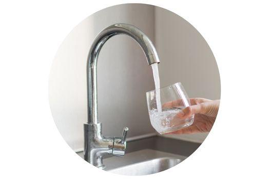 A hand holding a glass under a running faucet, filling it with water.