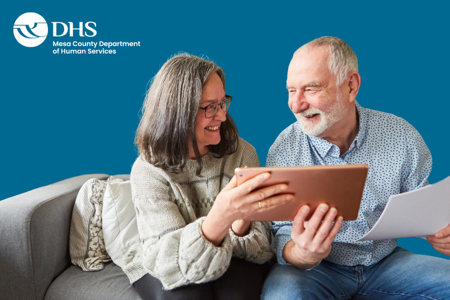Older adults working together on a tablet with MCDHS logo on blue background.