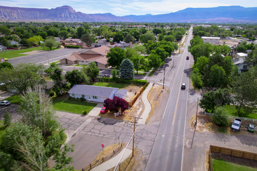 Aerial view of Orchard Avenue in Mesa County showing a residential neighborhood, mature trees, sidewalks and the roadway corridor extending toward the Grand Mesa in the distance.