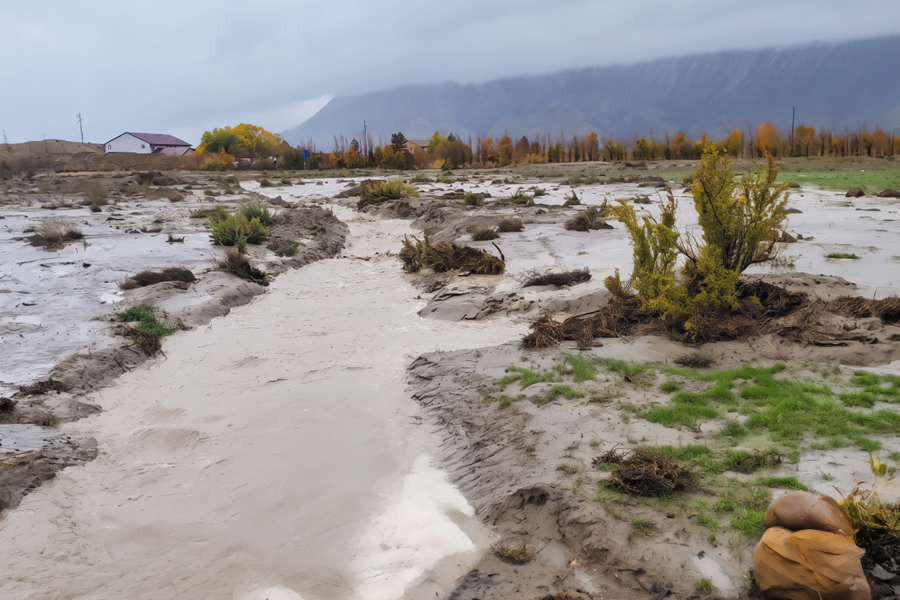 Muddy stormwater flow through Douglas Wash eroded bank and vegetation, with homes and the Book Cliffs in the distance. 
