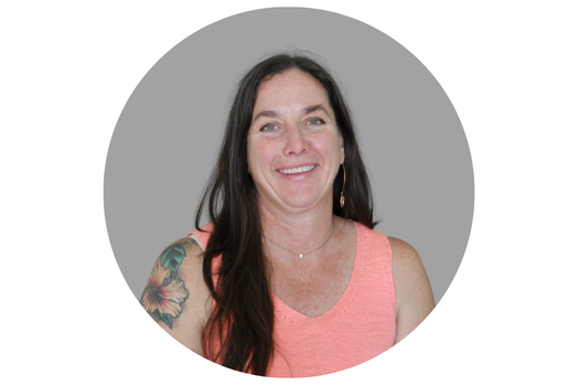 A woman with long dark hair, a hibiscus tattoo on her left arm, and a coral-colored tank top smiles at the camera. 